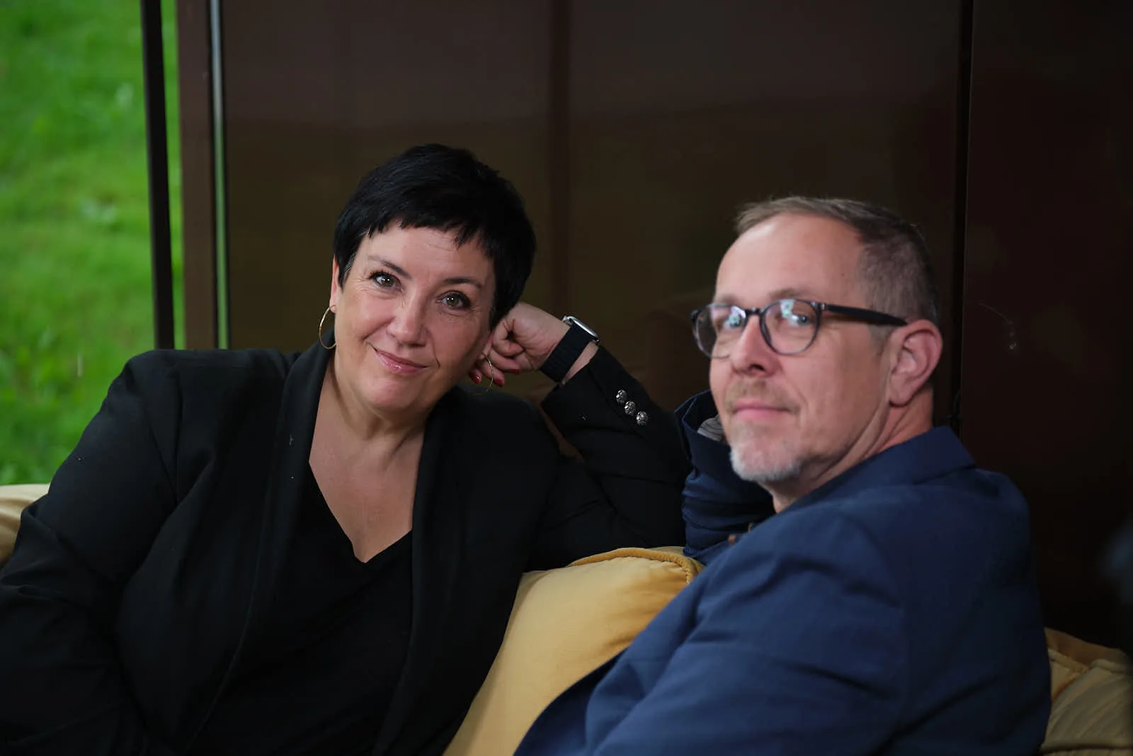 Wiebke und Ingo Anton sitzen zusammen auf dem Sofa und schauen in die Kamera
